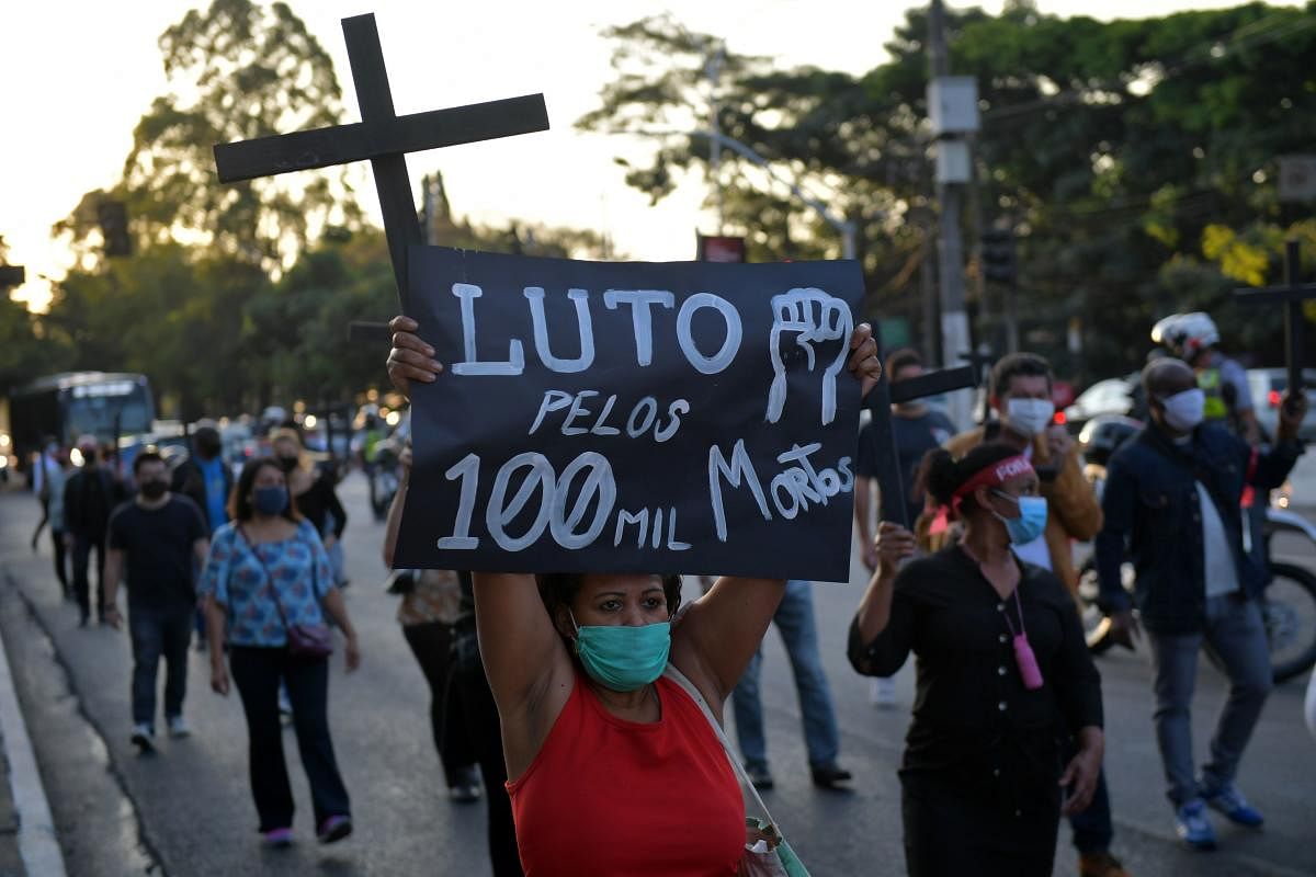 A health union member holds a cross and a sign reading “Mourning for the 100,000 dead” during a tribute to the nearly 100,000 victims of the novel coronavirus and to protest against Brazil's President Jair Bolsonaro. Credit: AFP