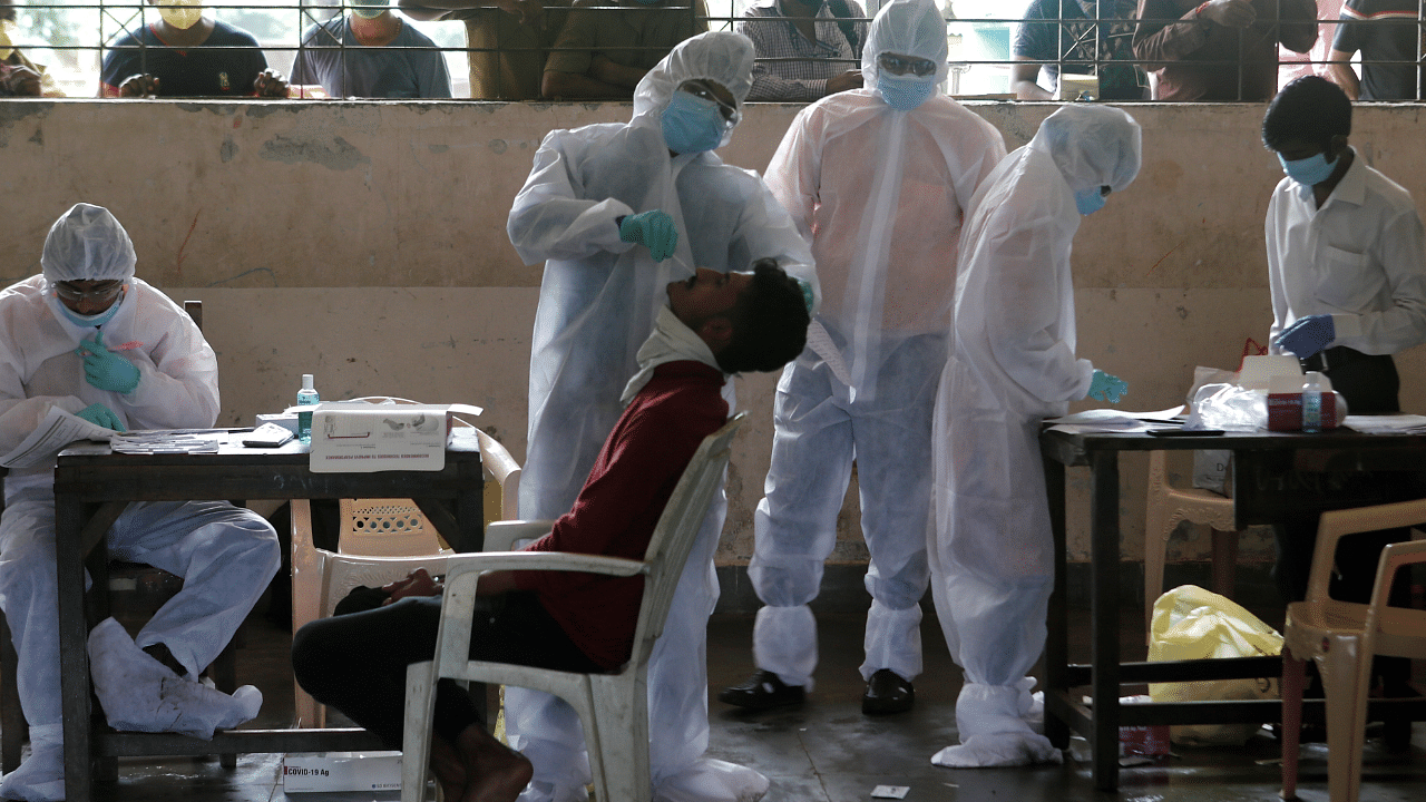 A health worker in personal protective equipment (PPE) collects a swab sample from a man as people outside wait for their test results during a rapid antigen testing check up campaign for the coronavirus. Credits: Reuters Photo