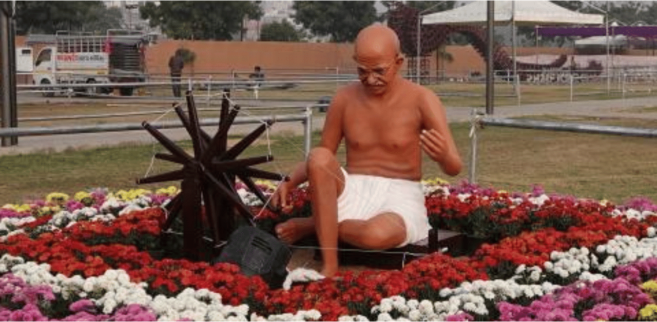 An statue of Mahatma Gandhi is pictured with a 'Charkha' or wooden spinning wheel in a bed of flowers. Credit: AFP Photo