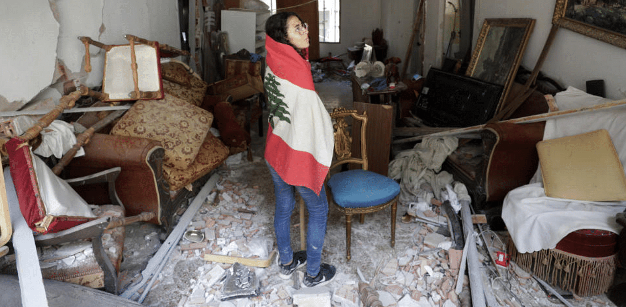 Farah Mahmoud, wrapped in Lebanese national flag, checks her parents destroyed apartment after Tuesday's explosion in the seaport of Beirut, Lebanon. Credit: AP