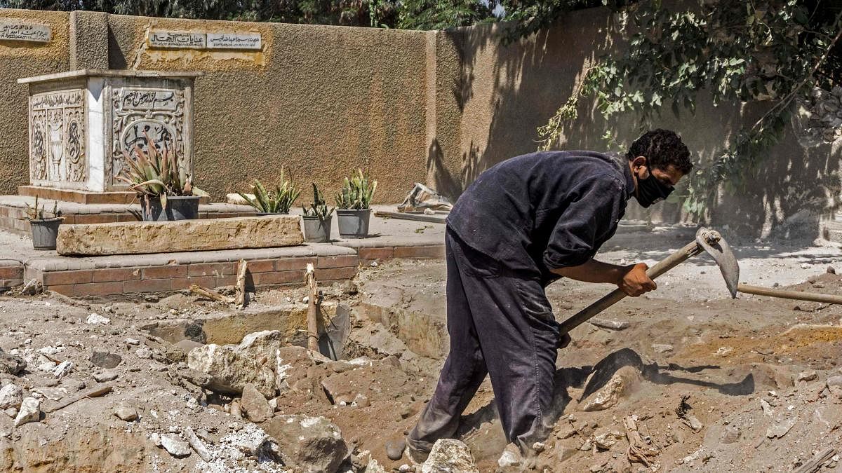 A worker, mask-clad due to the COVID-19 coronavirus pandemic, digs with a shovel during a cemetery demolition amidst ongoing roadworks at the historic City of the Dead necropolis. Credit: AFP