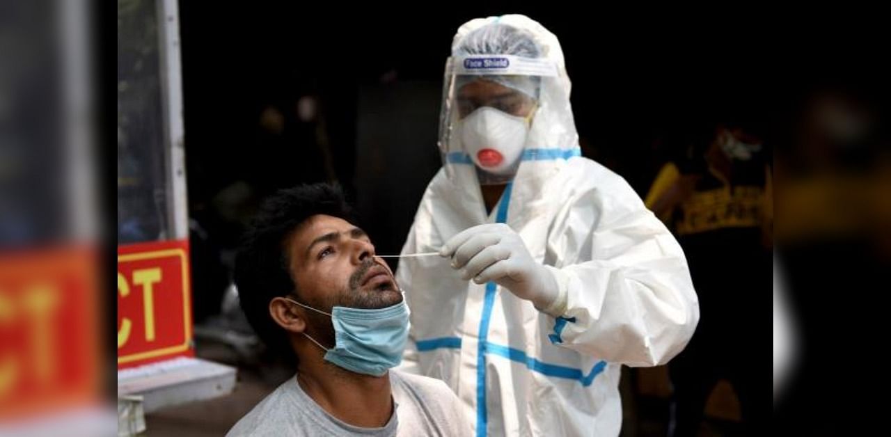 A health official wearing a Personal Protective Equipment (PPE) suit collects a swab sample from a man to test for the coronavirus. Credit: AFP