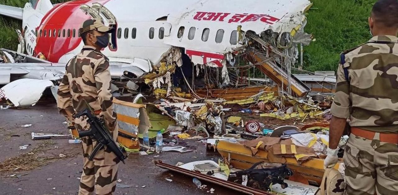 Security personnel stand guard near the mangled remains of an Air India Express flight, en route from Dubai, after it skidded off the runway while landing on Friday night, at Karippur in Kozhikode, Saturday, Aug. 8, 2020. (PTI Photo)