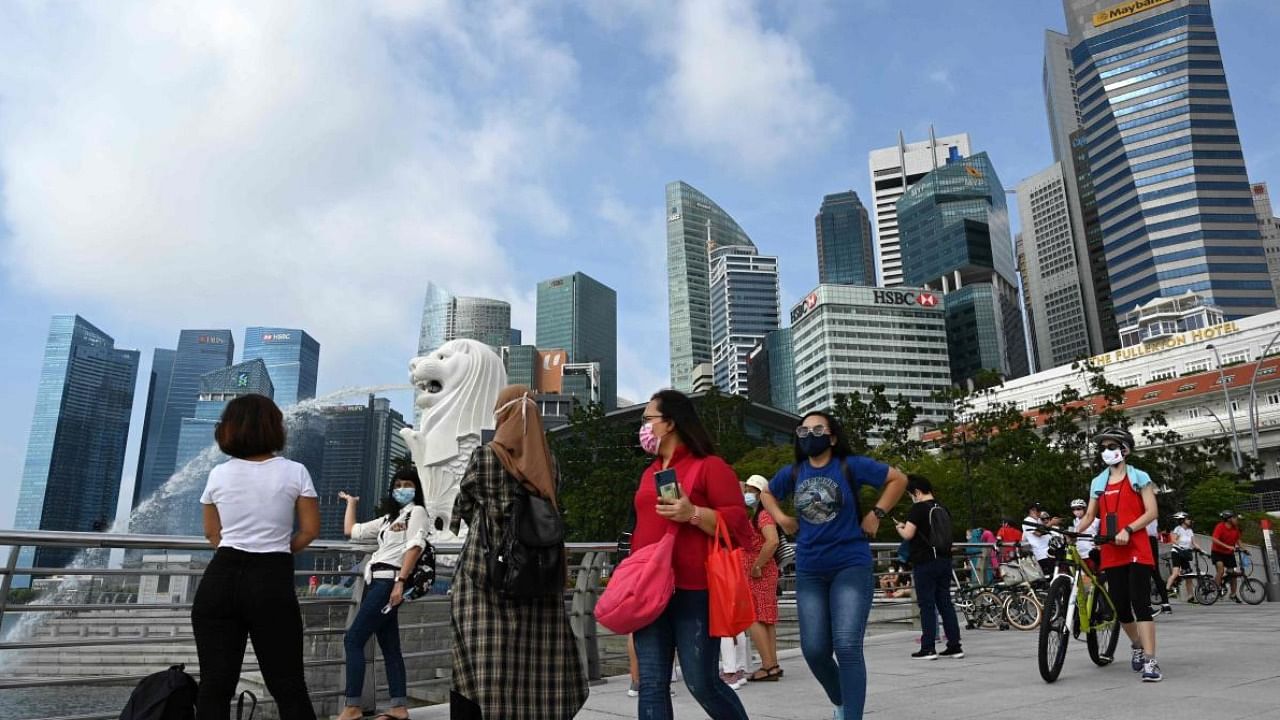 This photograph taken on August 9, 2020 shows people walking past the Merlion statue in Singapore. Credit: AFP