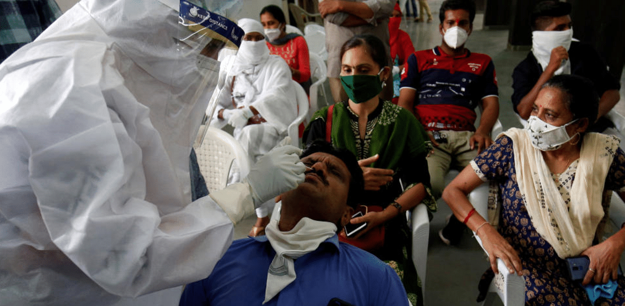 A healthcare worker wearing personal protective equipment (PPE) takes swab from a teacher of a municipal school for a rapid antigen test at a community center, amidst the coronavirus disease in Ahmedabad. Credit: Reuters Photo