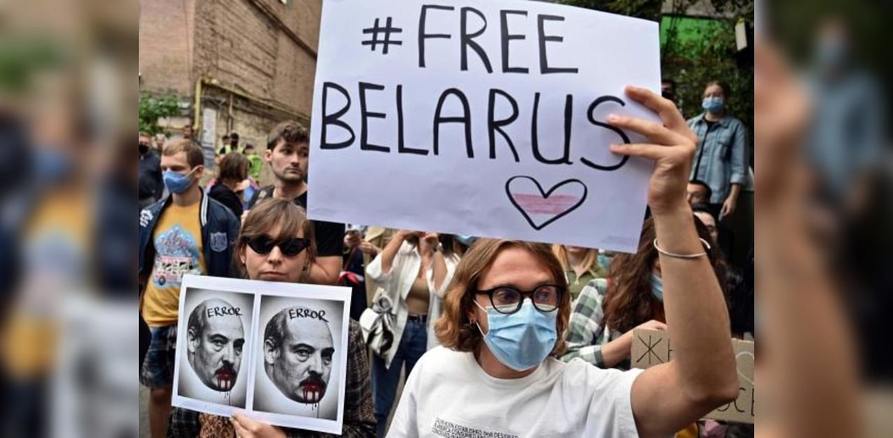 A member of the Belarus diaspora holds a placard depicting Alexander Lukashenko with blood on his mouth and moustache past another with a placard reading "#Free Belarus" as they with others take part in a rally in support of Belarus people protesting vote rigging in the presidential election, outside the Belarusian embassy in Kiev. Credit: AFP
