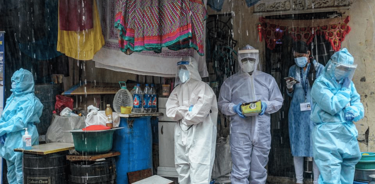 Health workers wearing PPE suits take shelter while conducting a Covid-19 screening under heavy rain in Mumbai on August 12. Credit: AFP Photo