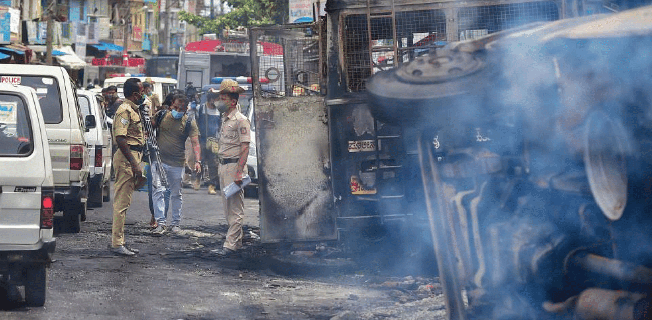Police stand guard next to charred remains of vehicles vandalised by a mob over a social media post, allegedly by a relative of a Congress MLA, in Bengaluru, Wednesday, Aug. 12, 2020. Credit: PTI Photo