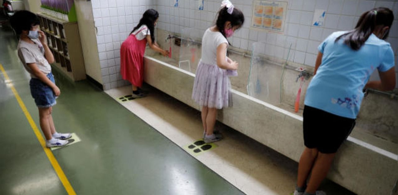 Students wearing protective face masks stand on marks for social distancing while they wash their hands amid the coronavirus disease. Credit: Reuters