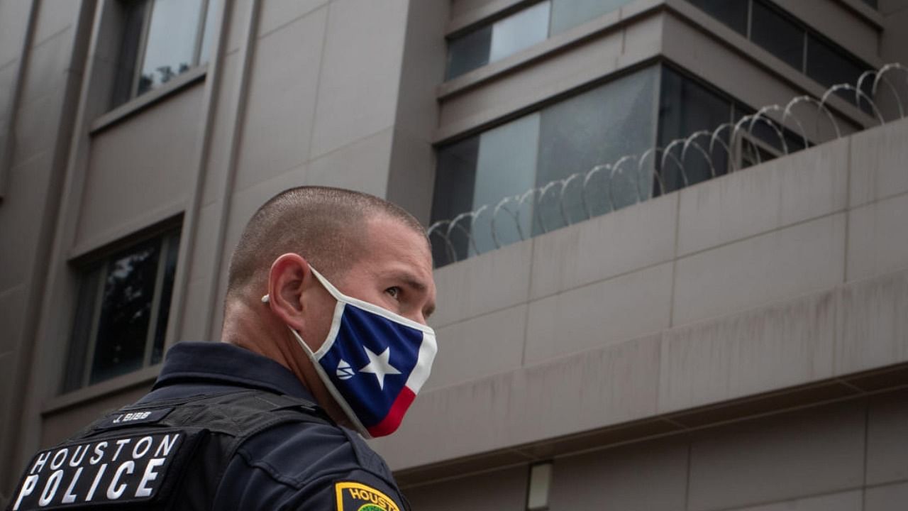 A police officer, wearing a mask with the colors of the Texas flag, stands guard outside China’s Consulate after Chinese employees left the building, in Houston, Texas. Credit: Reuters