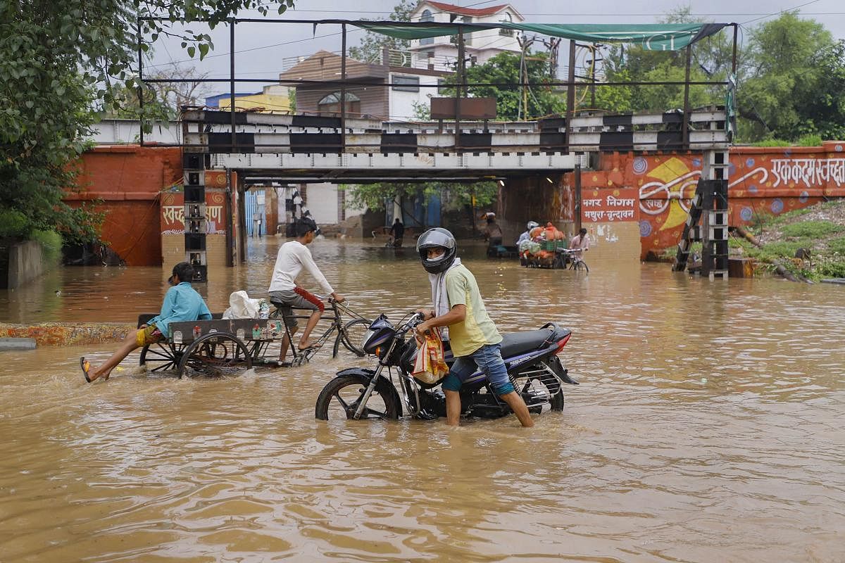 Commuters wade through a flooded street following heavy rainfall, in Mathura. Credit: PTI