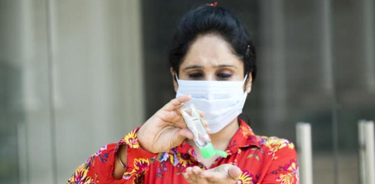 Woman wearing protective face mask cleaning her hands with sanitizer. Representative Photo. Credit: Getty Images