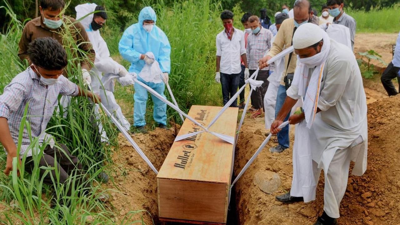 Relatives (in PPE) perform burial of a family member who succumbed to Covid-19, at a graveyard in New Delhi. PTI