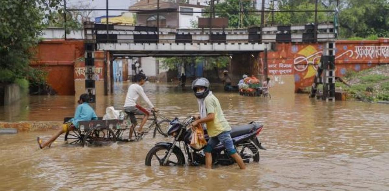 Commuters wade through a flooded street following heavy rainfall, in Mathura. Credit: PTI Photo