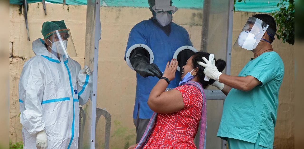 A health worker wearing personal protective equipment (PPE) gear collects a swab sample from a woman at a free Covid-19 coronavirus testing centre in Hyderabad. Credits: AFP
