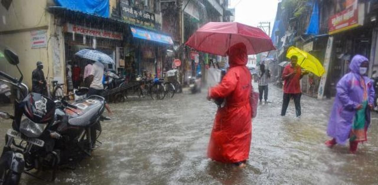 People wade through a waterlogged street during heavy rain, at Jambli Naka in Thane. Credit: PTI