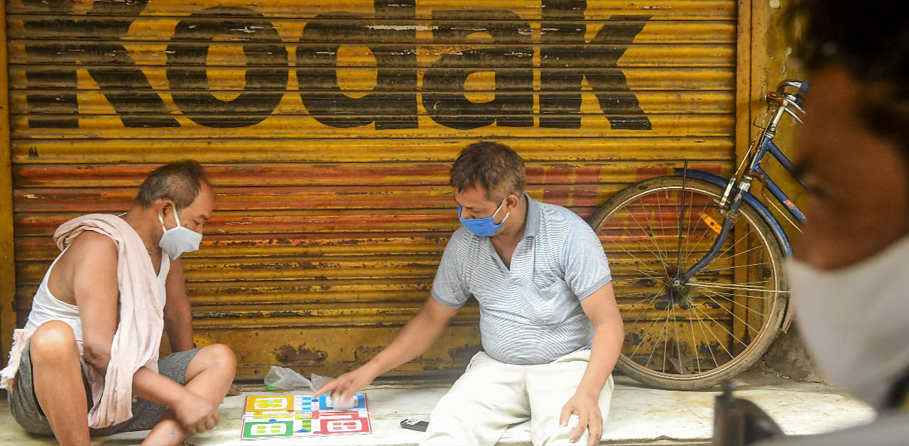 Labourers take a break from work as they play a board game sitting in front of a closed photo-studio shop. Credit: AFP