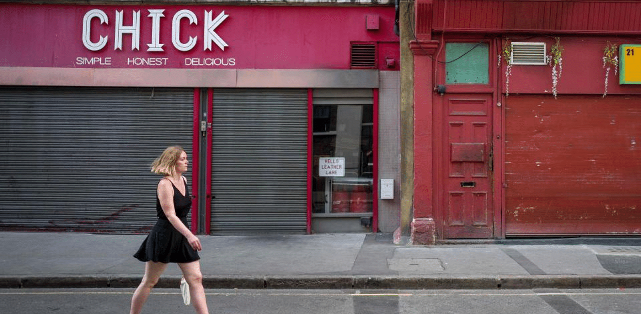 A pedestrian wearing a face mask or covering due to the Covid-19 pandemic, walks past shuttered shop fronts on an empty shopping street in London. Credit: AFP Photo