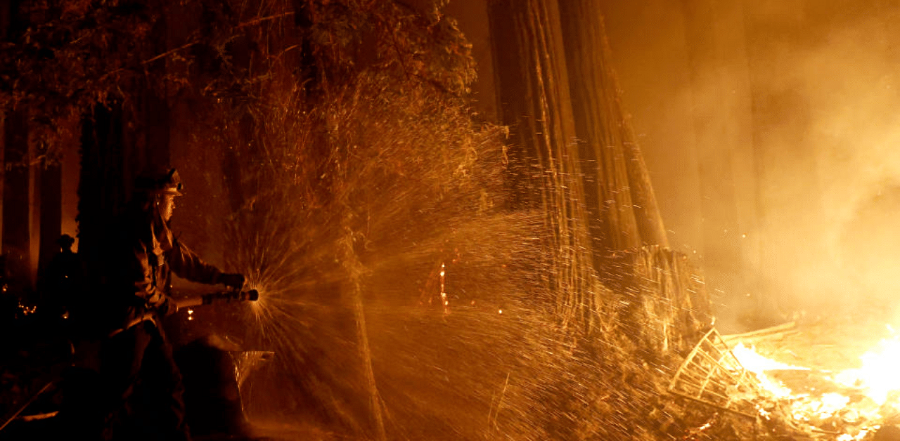 Cal Fire firefighter Anthony Quiroz douses water on a flame as he defends a home during the CZU Lightning Complex Fire in Boulder Creek, California, U.S. August 21, 2020. Credit: Reuters Photo
