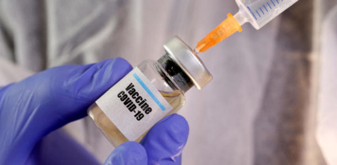 A woman holds a small bottle labeled with a "Vaccine Covid-19" sticker and a medical syringe. Credit: Reuters