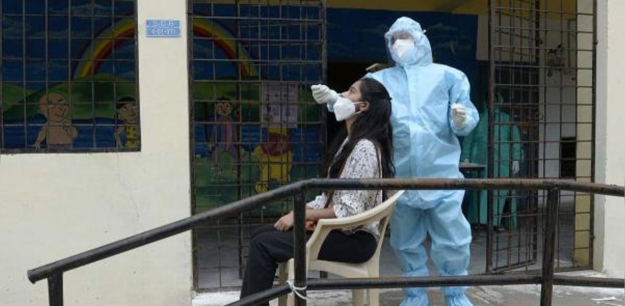 A health worker (R) wearing personal protective equipment (PPE) collects a swab sample from a resident at a free Covid-19 coronavirus testing centre. Credit: AFP