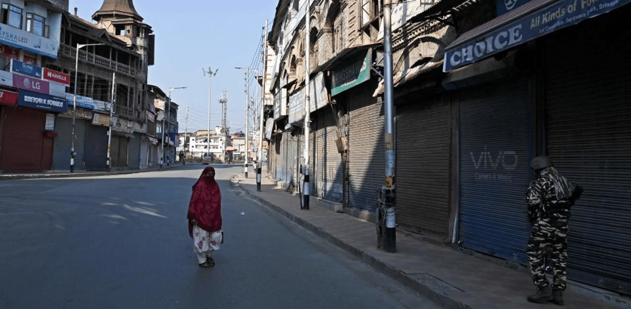 A woman walks along a street as security personnel stand guard during the one-year anniversary of the restive Kashmir region being stripped of its autonomy in Srinagar on August 5, 2020. Credit: AFP Photo