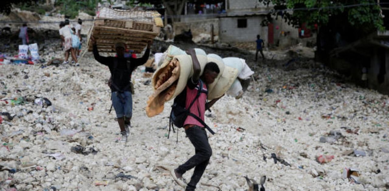 Men carry a bed and a mattress as they walk along an area affected by the passage of Tropical Storm Laura, in Port-au-Prince. Credit: Reuters