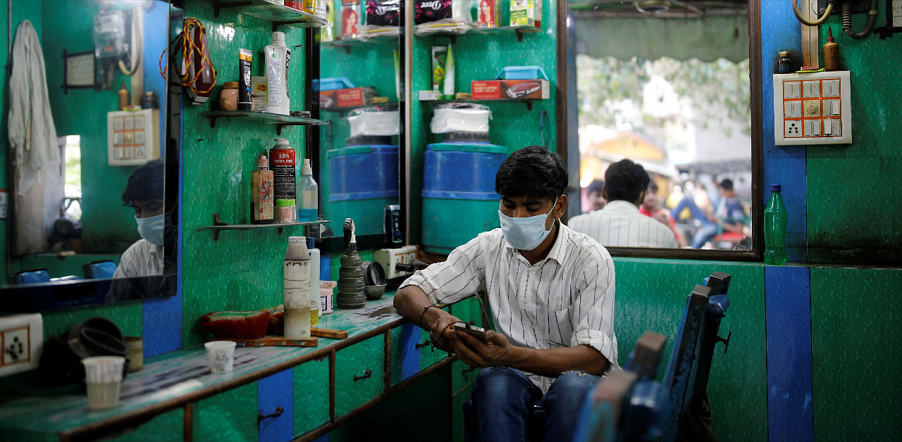 A barber wearing a protective face mask looks at his mobile phone as he waits for customers, amidst the spread of coronavirus disease (COVID-19), in the old quarters of Delhi, India. Credit: Reuters