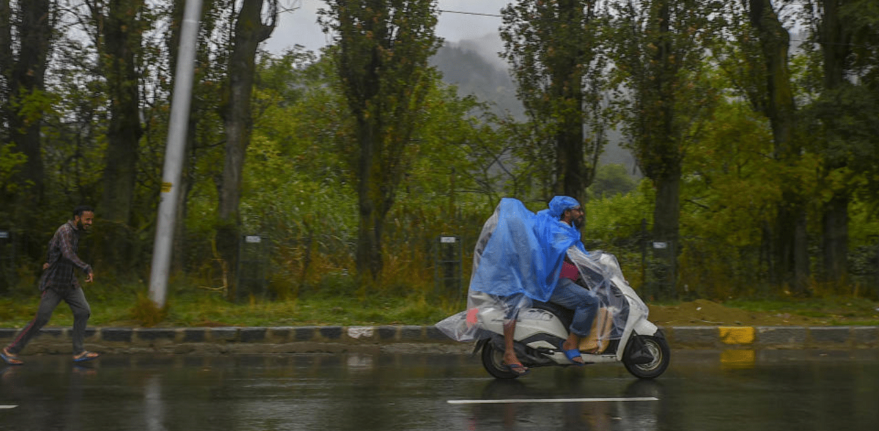  Men riding on a scooter cover themselves with a polythene sheet during heavy rain, in Srinagar. Credit: PTI