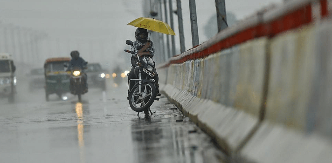  A motorcyclist holding an umbrella waits on a bridge for the rain to stop. Credit: PTI