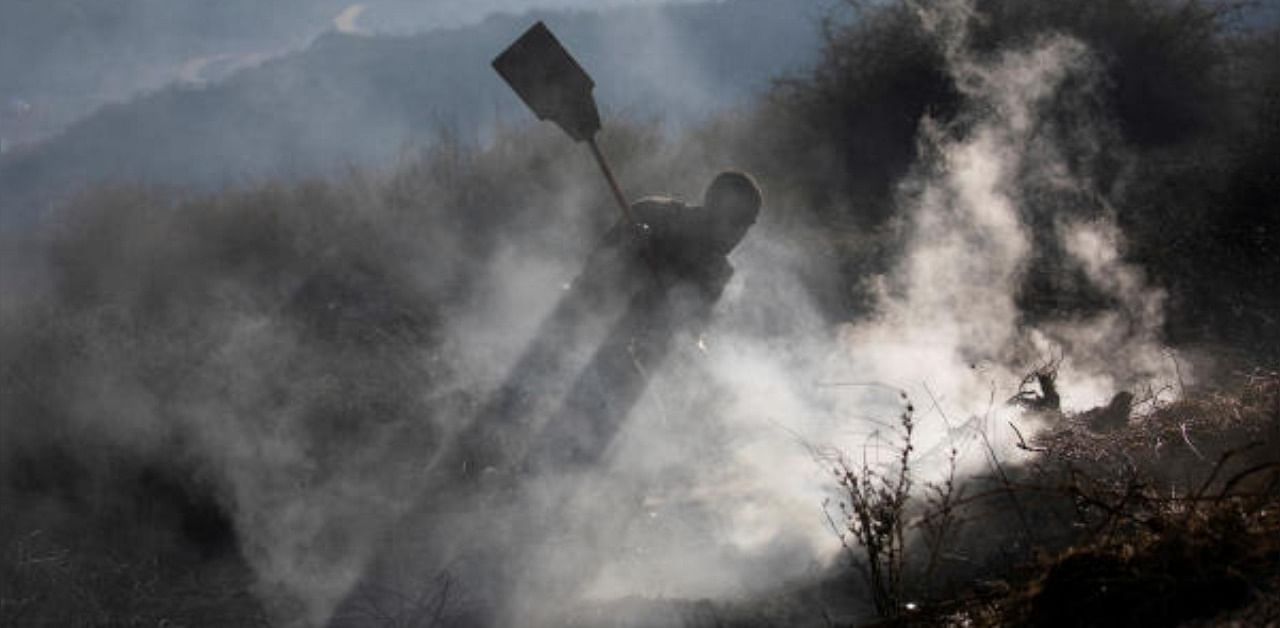 An Israeli soldier beats down smoke with a fire broom in an area that has seen blazes caused by fire balloons launched from the Palestinian enclave of Gaza. Credit: Reuters