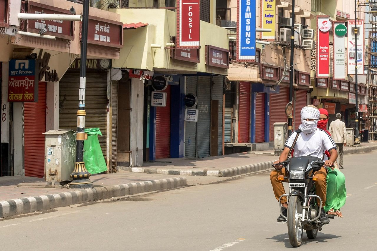 Motorists ride a motorbike past closed shops on a street after lockdown norms for weekends and public holidays in the state have been imposed as a preventive measure against the Covid-19. Credits: AFP Photo