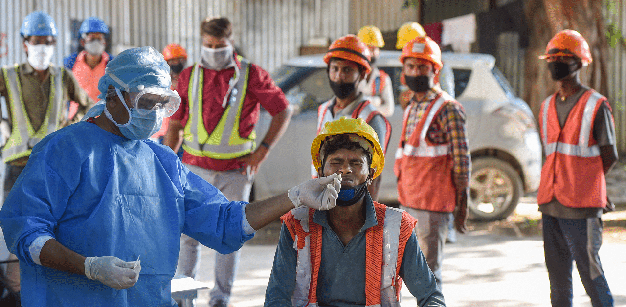 A health worker takes a sample from a construction worker for Covid-19 test as others wait for their turn. Credit: PTI Photo
