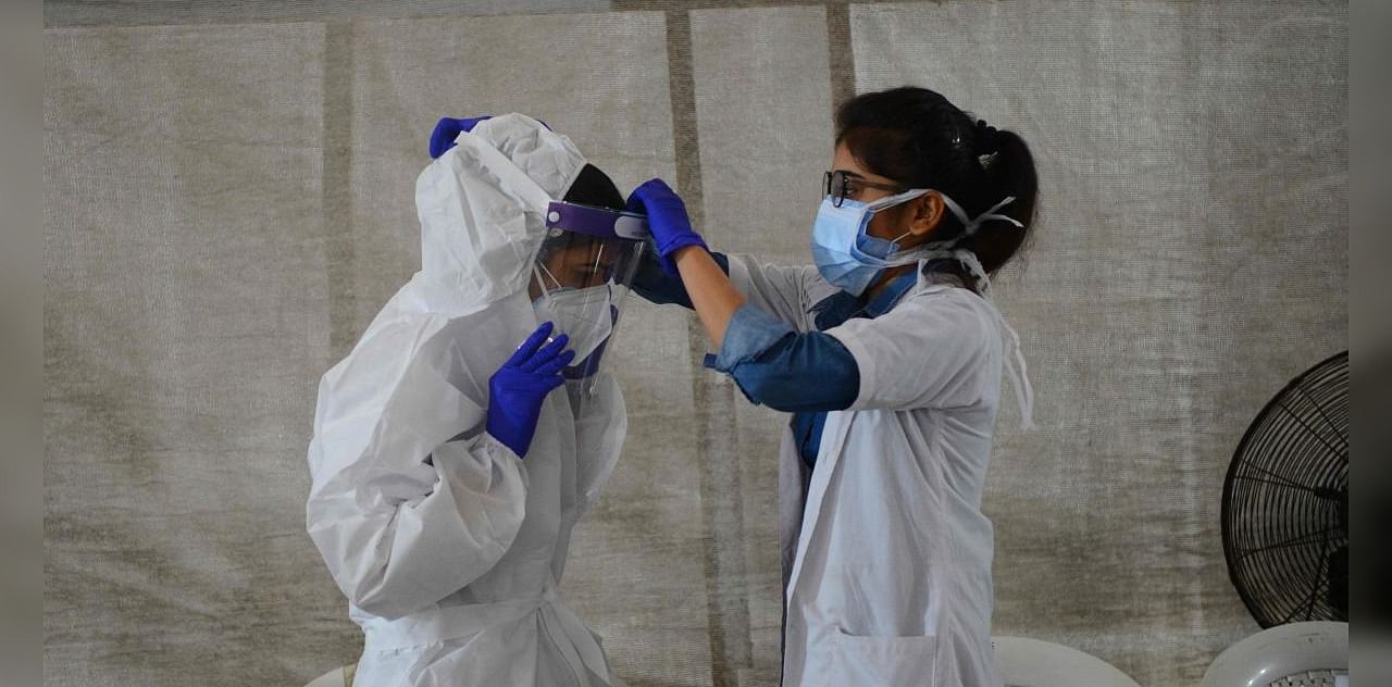 An health worker (L) is being helped by a colleague to wear a Personal Protective Equipment (PPE) as she prepares to conduct a Covid-19 coronavirus test of bus passengers at a testing camp in Sanathal, on the outskirts of Ahmedabad on August 30, 2020. Credit: AFP Photo
