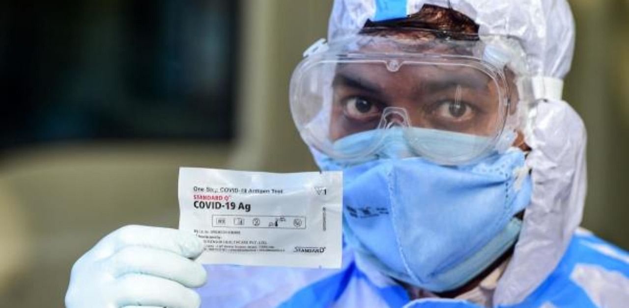 A health worker wearing a Personal Protective Equipment (PPE) suit shows a Rapid Antigen Test (RAT) kit for the Covid-19. Credit: AFP