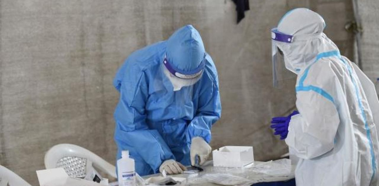 Health workers wearing Personal Protective Equiment (PPE) kits work on the collected swab samples for the Covid-19 at a testing camp. Credit: AFP