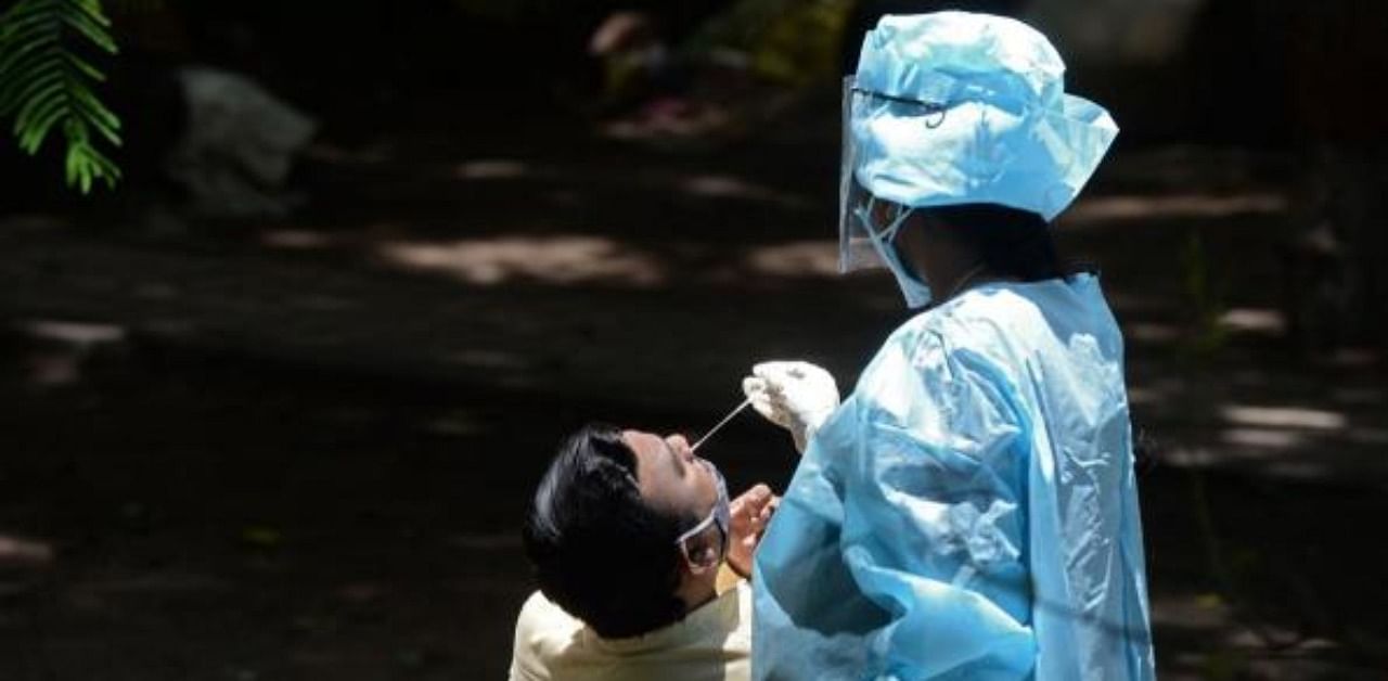 A health worker wearing Personal Protective Equipment (PPE) collects a swab sample from a man for a free Covid-19 test. Credit: AFP