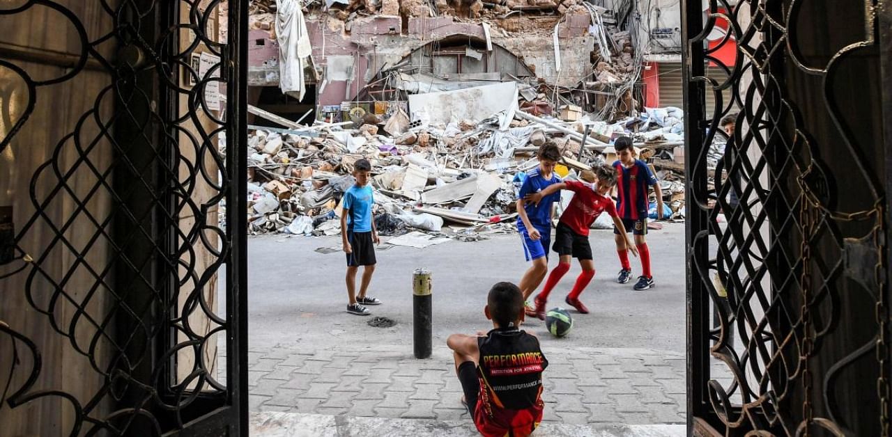 Children play with a football past rubble and destruction along a street in the Gemmayzeh district of Lebanon's capital Beirut. Credits: AFP