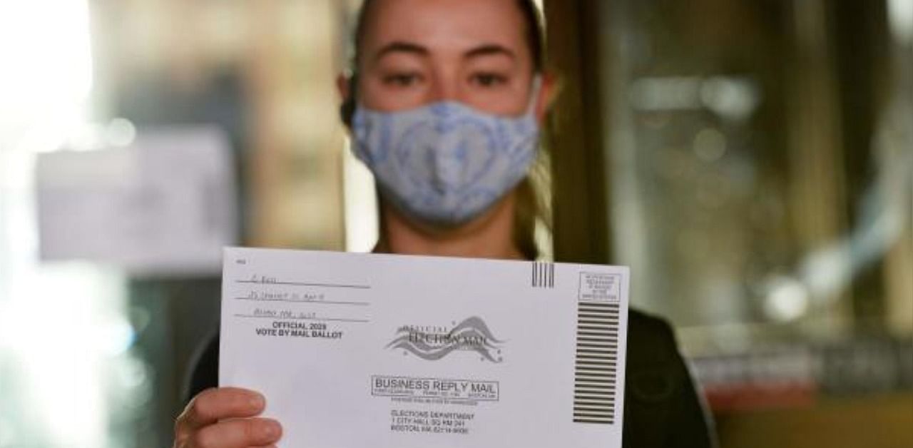 A woman holds up a mail-in ballot before dropping it off at Boston City Hall during the Massachusetts State Primary. Credit: AFP