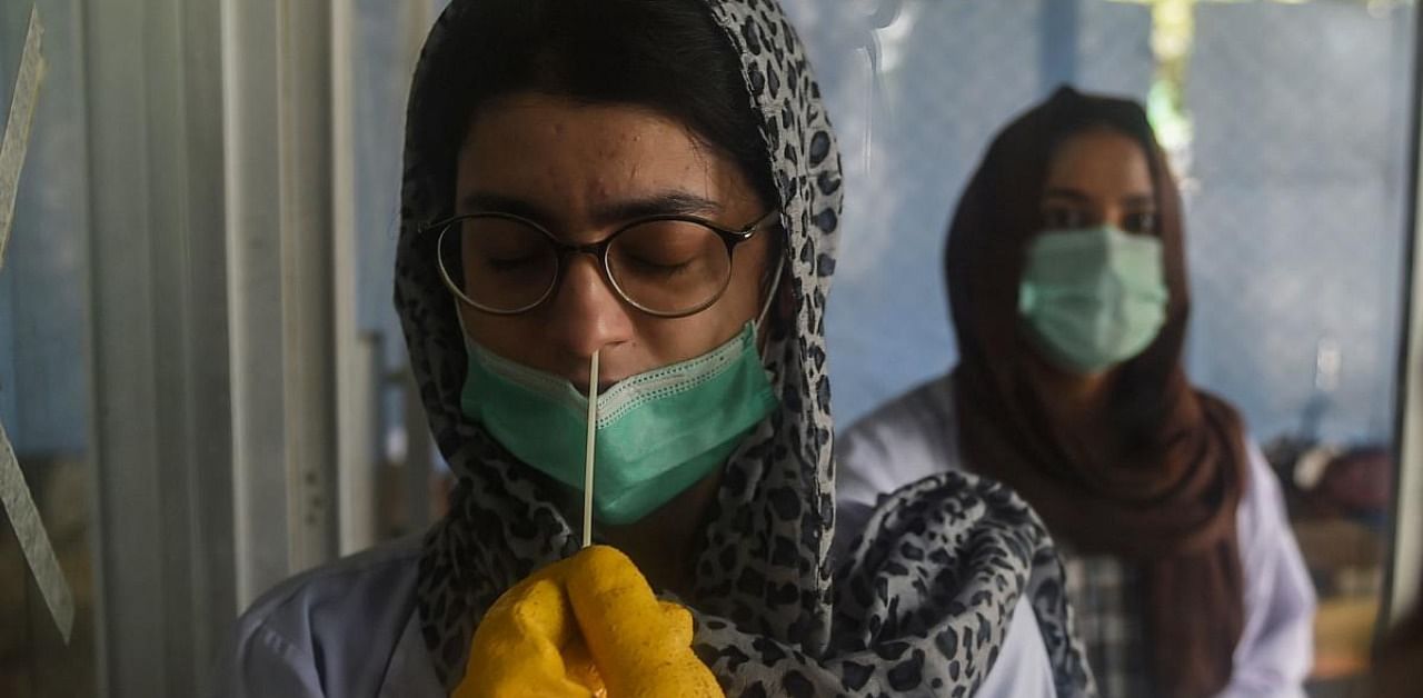 A health official takes a swab sample from a woman at a testing site in Karachi. Credits: AFP