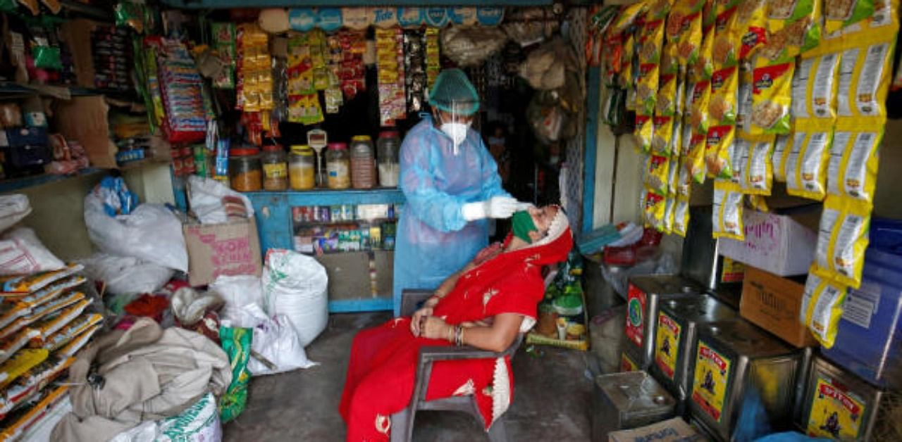 A healthcare worker wearing personal protective equipment (PPE) takes a swab from a woman for a rapid antigen test inside her grocery shop, amid the coronavirus disease. Credit: Reuters