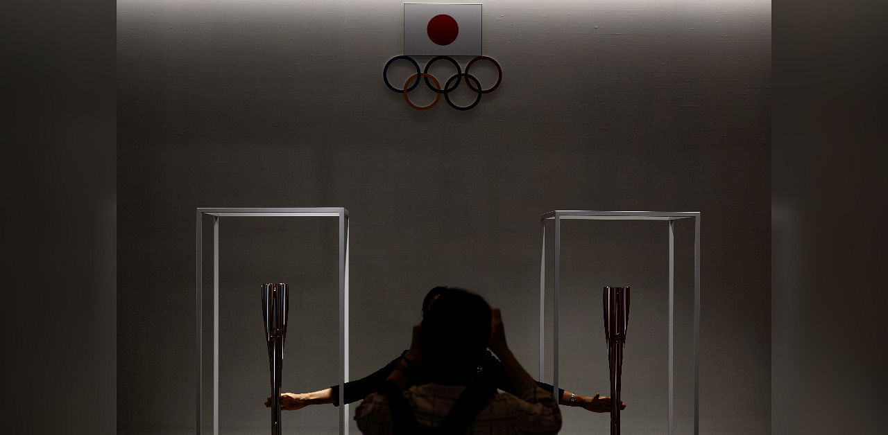 A visitor poses for pictures with the 2020 Tokyo Olympic relay torch (L) and Paralympic relay torch (R) at the Olympic Museum in Tokyo. Credit: AFP