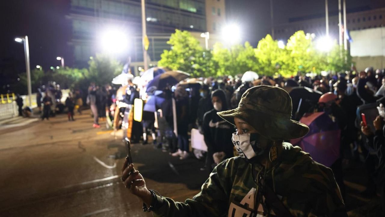 A woman wearing a George Floyd mask records a video during a standoff between demonstrators and police officers in front of the Public Safety Building after a peaceful march for Daniel Prude. Credit: AFP