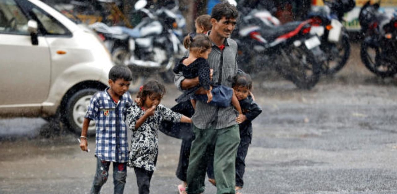 A man carrying children crosses a road during heavy rains in Ahmedabad, India. Representative Photo. Credit: Reuters