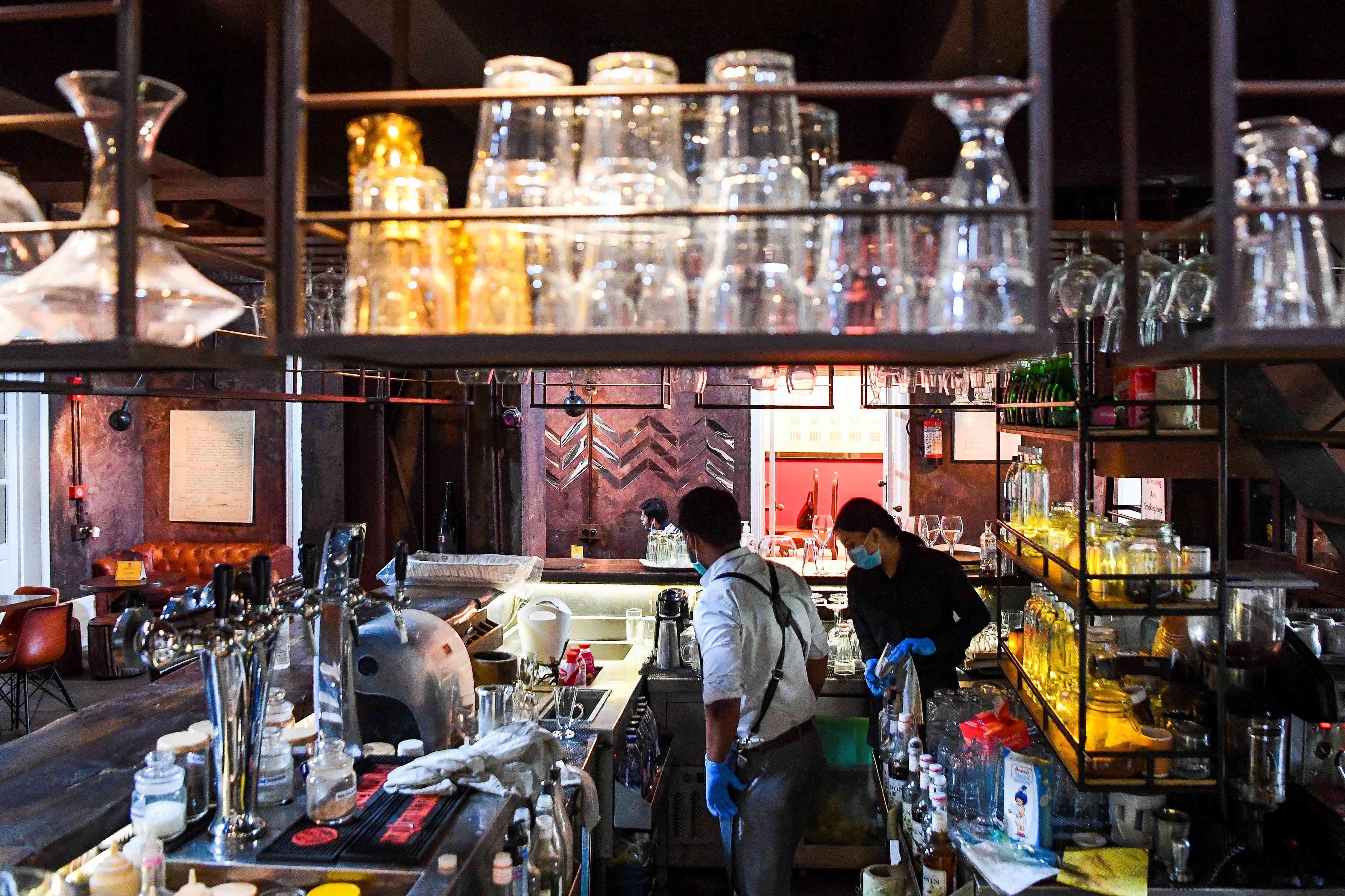Bartender Gagan (L) and a waitstaff clean their bar in a restaurant on the eve of the scheduled reopening of liquor bars in the capital, which were ordered shut due to the Covid-19 Coronavirus pandemic, in New Delhi on September 8, 2020. - Liquor bars will reopen in the capital from September 9 on a trial basis at fifty percent seating capacity. Credit: AFP Photo