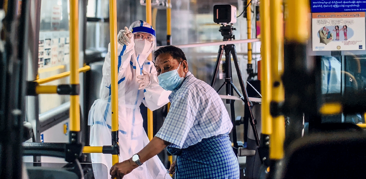 A health worker gestures to a man receiving a checkup on a mobile health clinic on a bus during a medical checkup and contact tracing campaign in Yangon. Credit: AFP Photo 