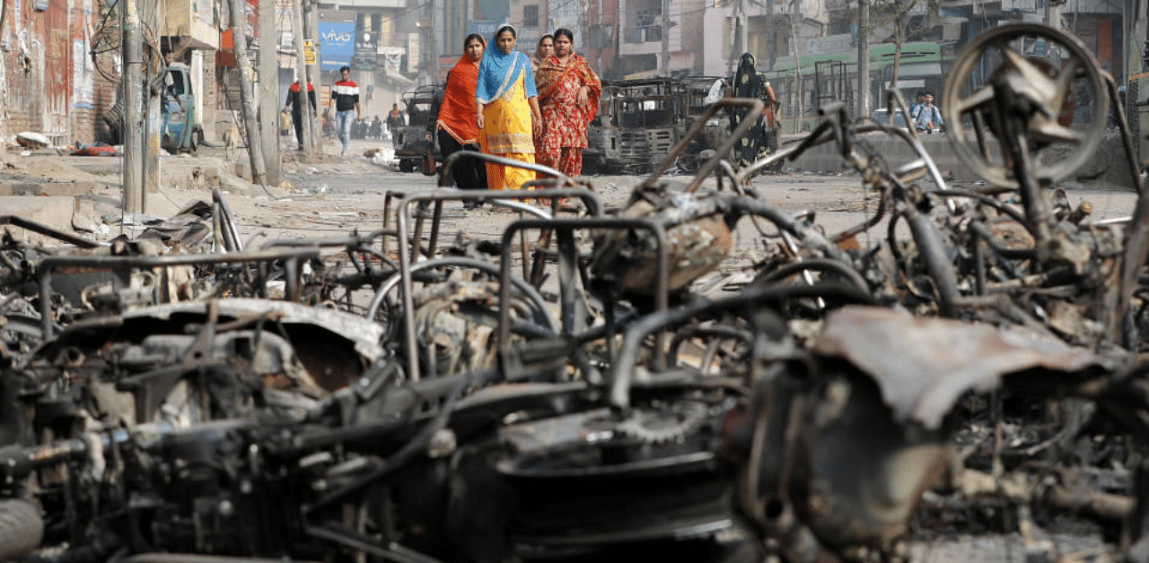 Women walk past charred vehicles in a riot affected area following clashes between people demonstrating for and against a new citizenship law in New Delhi. Credit: Reuters Photo