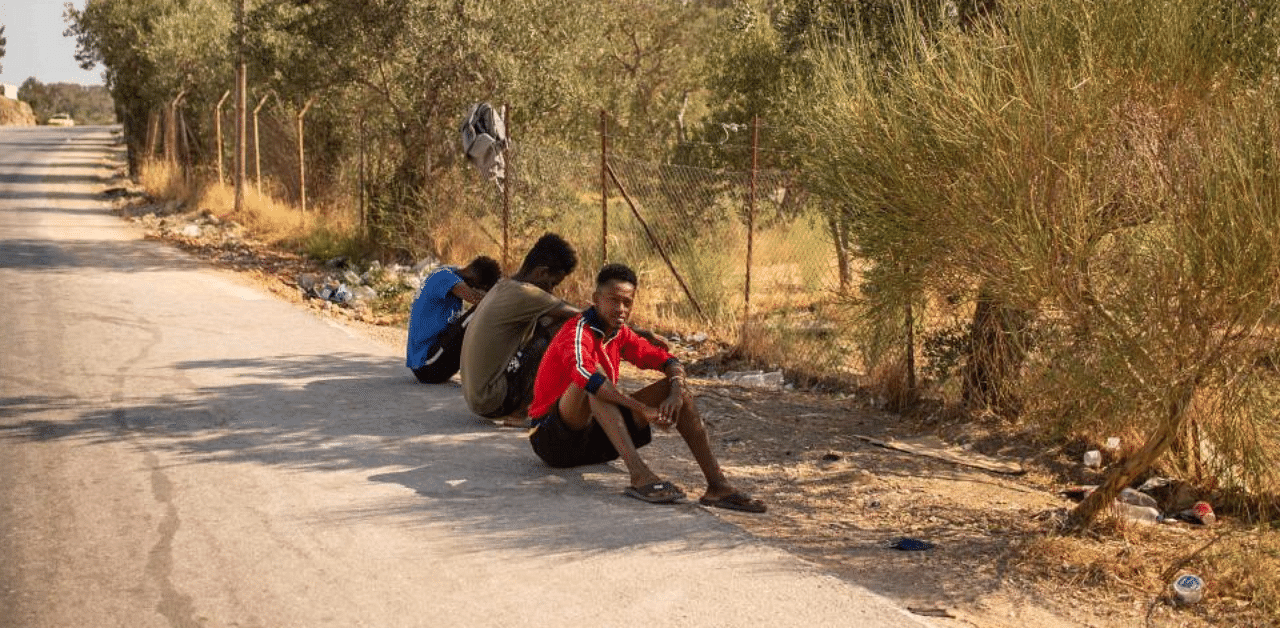 Migrants rest on the side of the road near the burnt Moria refugee camp, on the island of Lesbos. Credit: AFP
