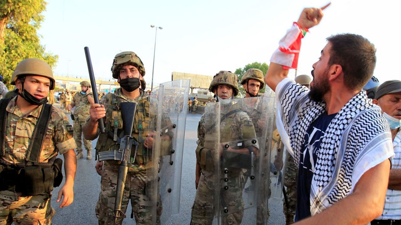 A demonstrator gestures as he stands near a Lebanese army soldier, during anti-government protests near presidential palace in Baabda. Credit: Reuters