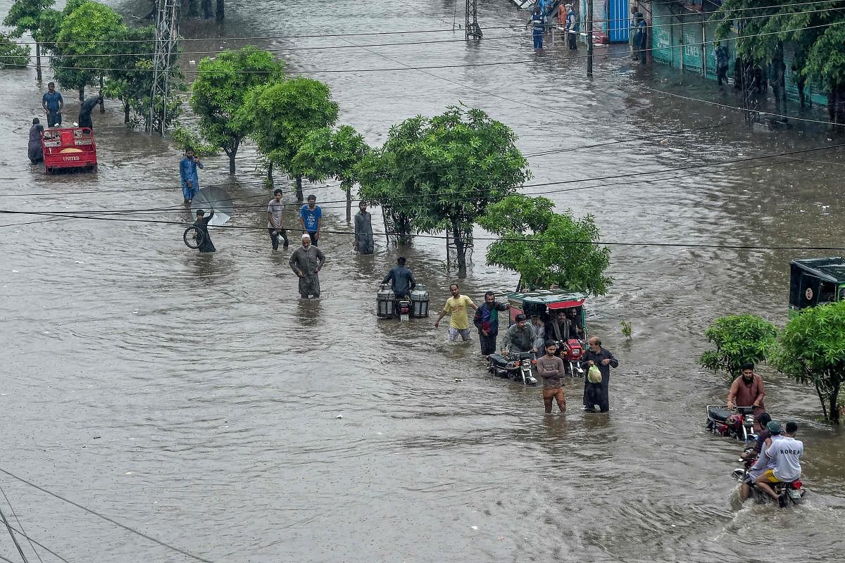 Motorists and pedestrians wade through a flooded street during heavy monsoon rains in Lahore. Credit: AFP